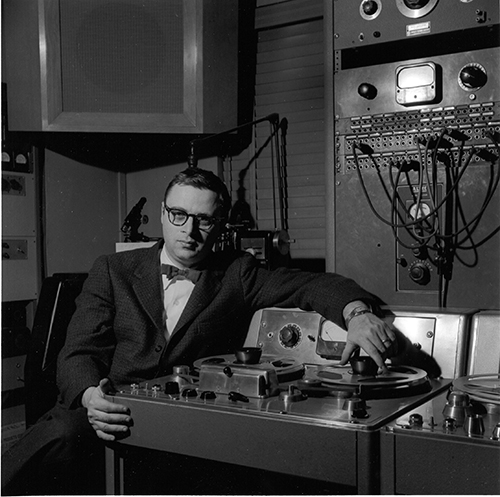 Man in suit and glasses with recording equipment. 