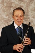 A man in a suit and tie smiles while holding a clarinet.