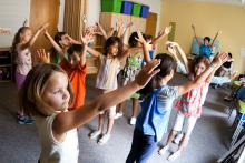Young children raise their hands above their heads as they take part in a dance class