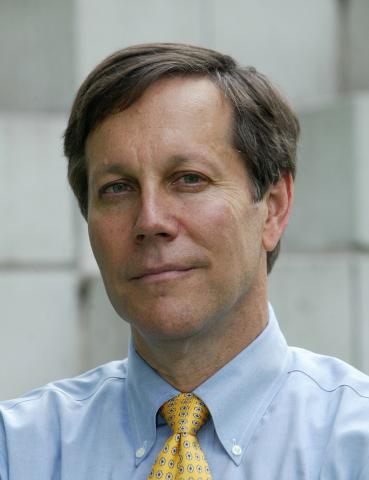 Portrait of white man with brown hair wearing a blue shirt and yellow tie. 