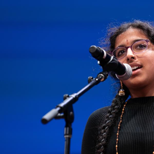 A young woman with glasses and two long braids speaks into a microphone