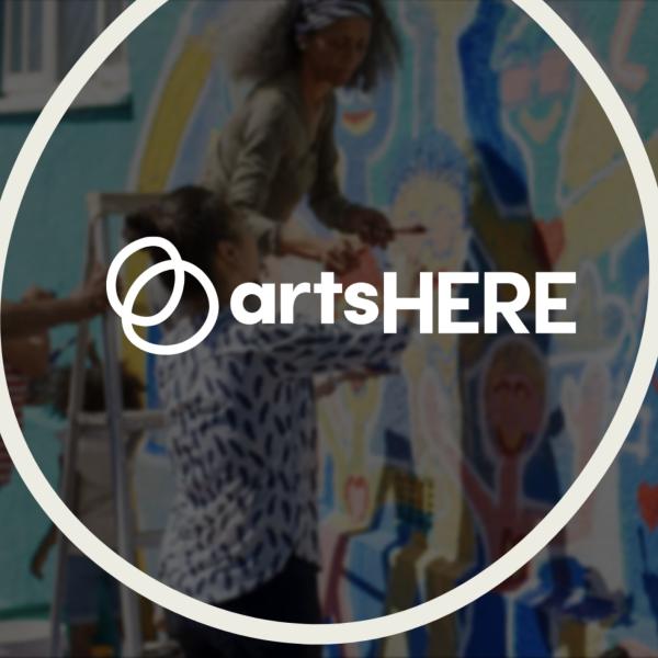 Circle ArtsHERE logo superimposed over a blurred background of people working on an outdoor mural